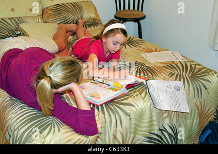 Mutter hilft ihr 2. Klasse Tochter Hausaufgaben auf dem Bett Stockfoto