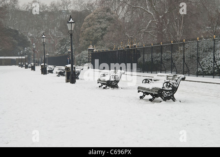 Eine Reihe von Parkbänken in mitten im Winter im Schnee draußen Kensington-Palast im Londoner Hyde Park bedeckt. Stockfoto