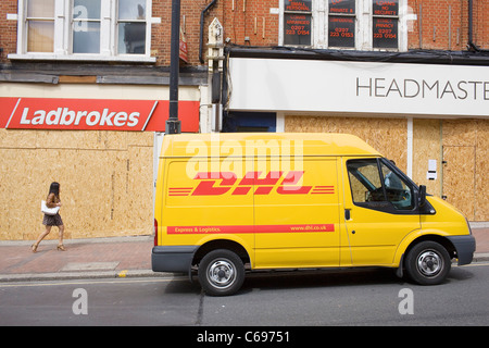 Eine Frau geht vorbei mit Brettern vernagelt Geschäfte in Clapham beschädigt in der August-Aufstand des Jahres 2011. Stockfoto