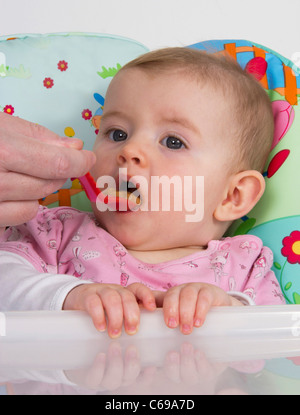Niedlichen Mädchen sitzen im Hochstuhl mit pürierte Nahrung gefüttert Stockfoto