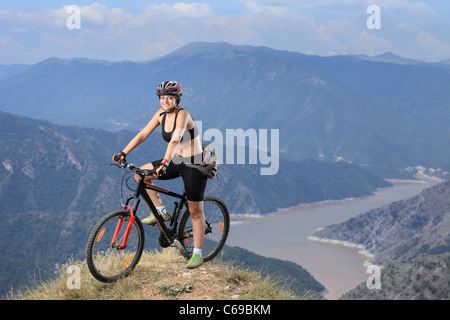 Ein Weibchen posiert mit einem Mountain-Bike mit See im Hintergrund Stockfoto