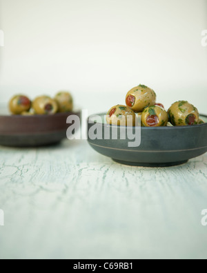 Grüne Oliven gefüllt mit Paprika mit Olivenöl und Kräutern in einem Topf Stockfoto