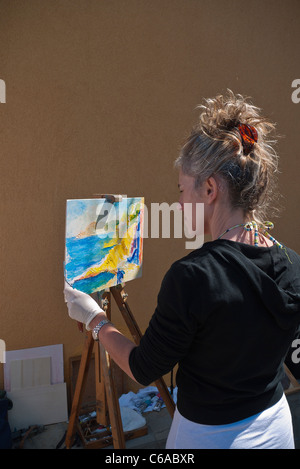 Ein weiblicher Öl Maler malt eine Meereslandschaft auf einer Staffelei montiert Leinwand in den Cinque Terre, Italien Stadt von Riomaggiore. Stockfoto