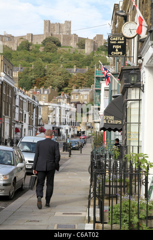 Mann zu Fuß durch Fisch & Chips Shop in Dover, mit der Burg im Hintergrund. Kent England UK Stockfoto