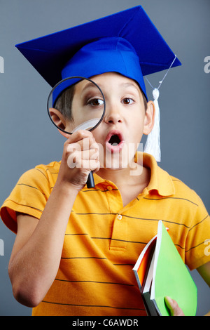 Porträt von neugieriger Junge im Abitur Hut Blick durch die Lupe Stockfoto