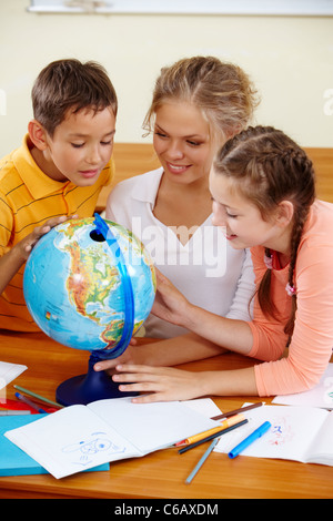 Porträt von niedlichen Schüler und Lehrer betrachten Globus im Klassenzimmer Stockfoto