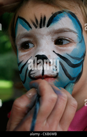 Ein junges Mädchen suchen Sie aufmerksam, während ein Künstler malt ihr Gesicht auf einem Kinderfest in Leipzig, Deutschland Stockfoto