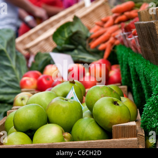 Schuss von grünen Äpfeln in einem Apple-Box auf einem Marktstand mit roten Äpfeln und Karotten im Hintergrund schließen Stockfoto