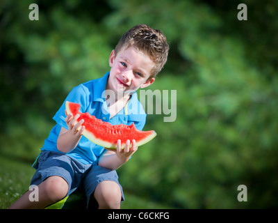 Fröhlicher Junge draußen essen ein Stück Wasser Melone Stockfoto