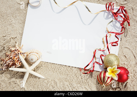 Weihnachtskugeln und Muscheln mit leeren Karte am Strand. Stockfoto