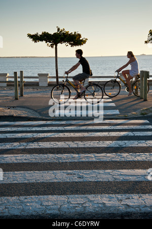 Der Strand bei Saint Georges De Didonne, Charente-Maritime, Frankreich. Radfahrer fahren entlang der Strandpromenade in der Nähe von einem Zebrastreifen Stockfoto