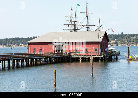 alten Wharf am Penn Bucht mit Masten zwei Großseglern sichtbar über dem Dach des malerischen roten hölzernen Schindeln Gebäude Coupeville Stockfoto