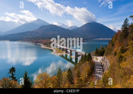 Reflexionen einer Straße Brücke über See Sylvensteinspeicher, mit Bergen im Hintergrund, in Bayern, Deutschland Stockfoto