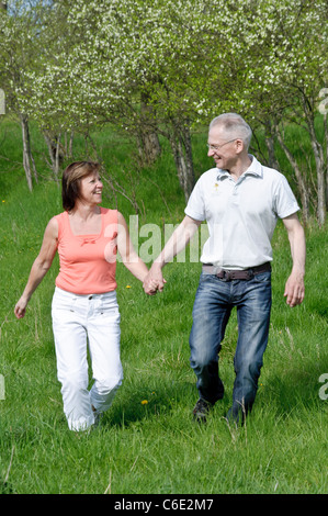 Paar mittleren Alters gehen Hand in Hand auf einer Wiese Stockfoto