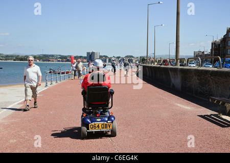 Ältere Menschen mit einem Mobilität scooter auf der Strandpromenade. Morecambe, Lancashire, England, Großbritannien, Großbritannien Stockfoto