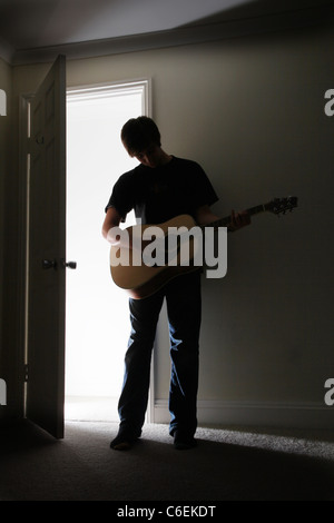 Junger Mann stehend in einem dunklen Raum eine akustische Gitarre zu spielen. Stockfoto