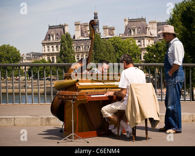 Zwei Musiker spielen verschiedene Instrumente auf einer Brücke im Zentrum von Paris. Ein Mann beobachtet sie. Stockfoto