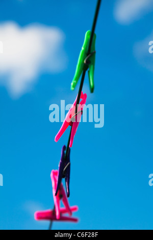 Eine Reihe von bunten Wäscheklammern hängt eine Wäscheleine gegen einen blauen Sommerhimmel. Stockfoto