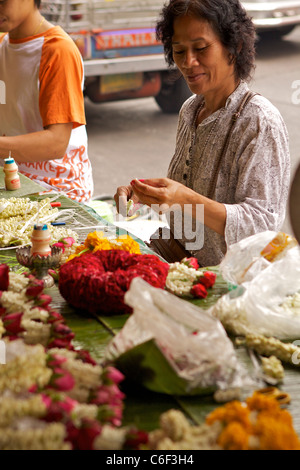 Eine Frau schafft Jasmin und Ringelblume "Phuang Mulai' - Thai Blumenkranz auf einem Straßenstand in Pak Klong Talat-Markt Stockfoto