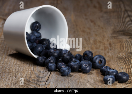 Heidelbeeren, die Tasse auf hölzernen Hintergrund aus einer fiel überrollen Stockfoto