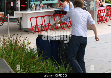 Rückansicht eines männlichen werfen Müll in einem Wheelie bin am Ufer der Themse Stockfoto