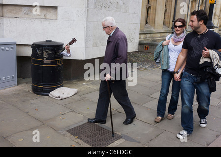 Eine Straße Straßenmusiker versteckt in einem Abfallbehälter, zusätzliches Geld zu verdienen, wie Passanten seine Musik auf einem Cambridge-Pflaster hören. Stockfoto