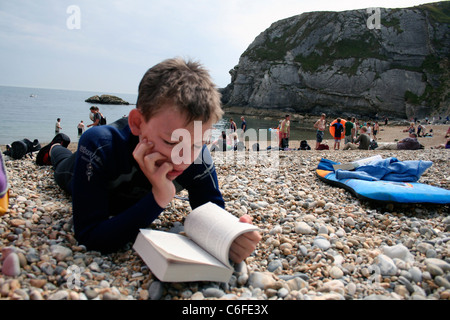 Junge 14 im Neoprenanzug lesen am Strand, Durdle Door Jurassic Coast in der Nähe von Lulworth in Dorset, England Stockfoto