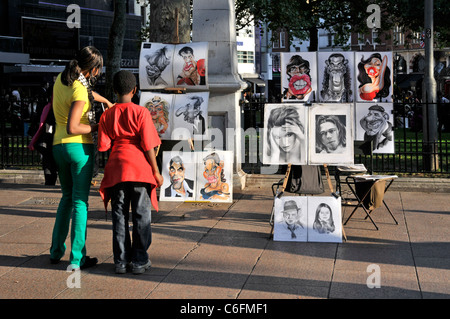 London Sommer Straße Szene zurück Blick auf die Menschen die Karikatur artwork portrait Skizzen im sonnigen Leicester Square London West End England Großbritannien Stockfoto