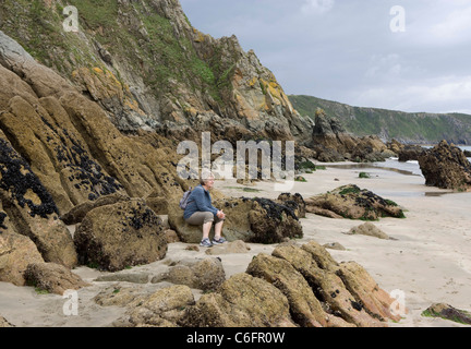 Eine Dame sitzt auf den Felsen an einem Sandstrand am Gorran Haven Cornwall Stockfoto