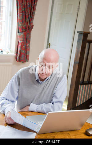 Älterer Mann bezahlt seine Rechnungen online, vor seinem Laptop sitzt Stockfoto