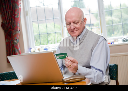 Reifer Mann, selbstbewusst und sicher bezahlt seine Rechnungen online mit einer Kreditkarte Stockfoto