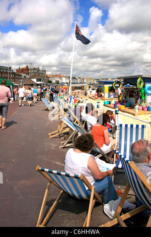 Leute sitzen in Liegestühlen auf Weymouth Strandpromenade Dorset Stockfoto