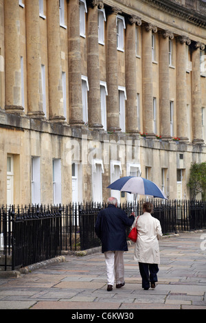 Reifes Paar, das im August in Bath, Somerset, Großbritannien, unter einem Regenschirm entlang des Royal Crescent läuft Stockfoto