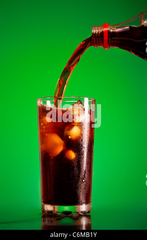 Cola in Glas gießen, auf grünem Hintergrund