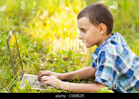 Schuljunge mit seinem Laptop im Freien auf einer Wiese Stockfoto