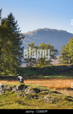 Eine asiatische Frau sitzt und genießt die Aussicht auf eine Wanderung in den Lake District, UK Stockfoto