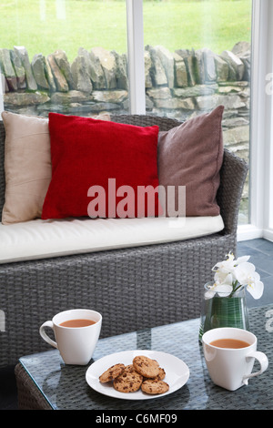 Tee oder Kaffee und Gebäck in einem Wintergarten mit Rattanstühlen und modernes design Stockfoto