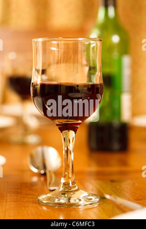 Glas Rotwein auf einen Esstisch mit einer Flasche Wein und mehr Gläser im Hintergrund Stockfoto