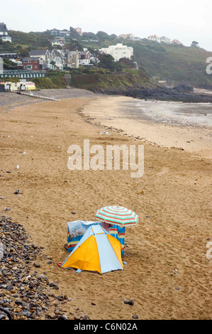 Ein einsamer entschlossene Urlauber baut einen Unterschlupf vor dem Regen am leeren Strand von Langland Bucht in der Nähe von Swansea zu decken. Stockfoto