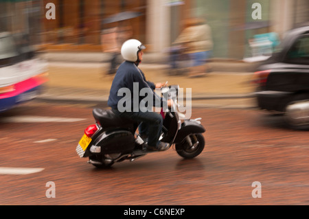 Ein Mann auf einem Roller fährt durch die Stadt und zeigt absichtlich Bewegungsunschärfe in Norwich, Norfolk, England, Großbritannien, Uk Stockfoto