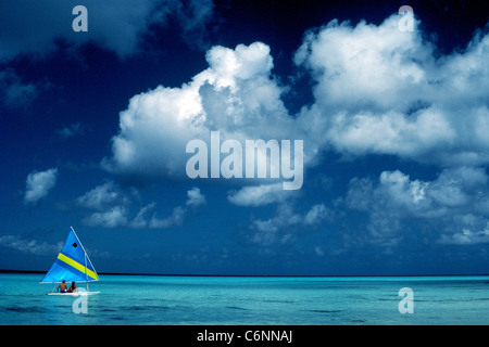 Ein kleines Segelboot mit zwei Urlauber gleitet über das türkisblaue Karibische Meer unter geschwollenen weißen Wolken und einem lebhaften blauen Himmel in Cozumel, Mexiko. Stockfoto