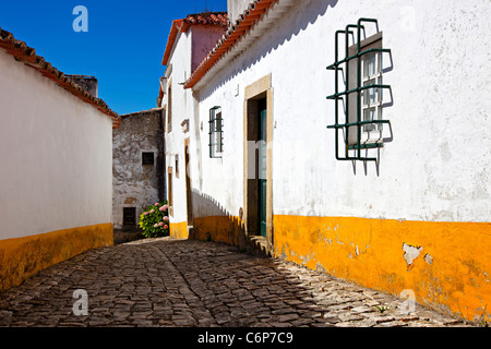 Schmalen gepflasterten Straße in alten mittelalterlichen Dorf Obidos, Portugal. Häuser mit weißen Wänden und gelben Streifen. Stockfoto