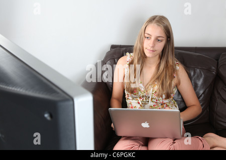 Mädchen mit Laptop und vor dem Fernseher sitzen auf einem Sofa. Stockfoto