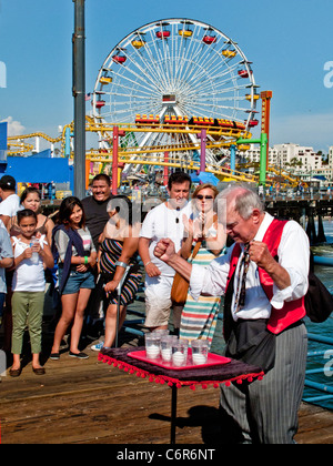 Ein älterer Magier führt einen verschwindenden Ei-Trick für sein Publikum im Vergnügungspark am Santa Monica Pier. Stockfoto