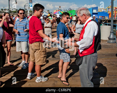 Ein älterer Magier sammelt Beiträge in einen Hut von seinem Publikum nach einem Auftritt am Santa Monica Pier. Stockfoto