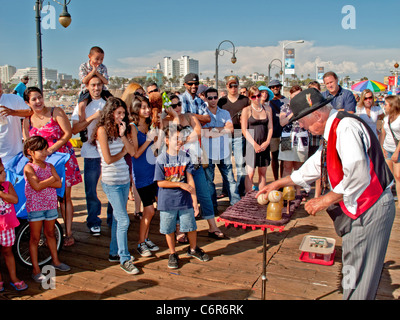 Ein älterer Magier führt einen Tasse und Baseballs Trick für sein Publikum im Vergnügungspark am Santa Monica Pier. Stockfoto