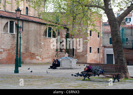 Eine Frau schläft auf einer Bank, Weg von den Touristen auf einem Platz in Venedig, Italien Stockfoto