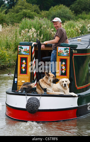 Ein Narrowboater mit seinen Hunden auf einem traditionell gebauten Handwerk am Oxford-Kanal in der Nähe von Braunston, Northamptonshire. Stockfoto