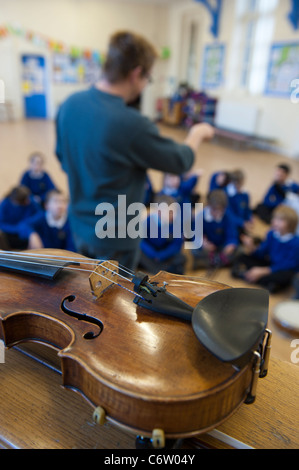 Eine Geige im Vordergrund, während ein Lehrer eine Musikstunde, Grundschüler führt. Stockfoto