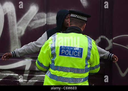 Junge schwarze Mann trägt einen Hoodie wird angehalten und durchsucht eine Metropolitan Police Officer bei Notting Hill Carnival in London Stockfoto